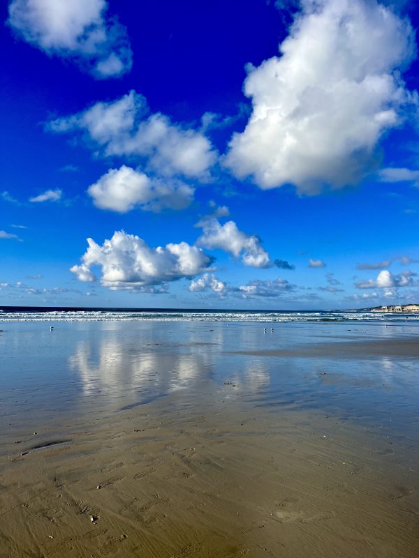 Partly cloudy blue sky at a low tide ebb with reflections of the clouds in wet sand 